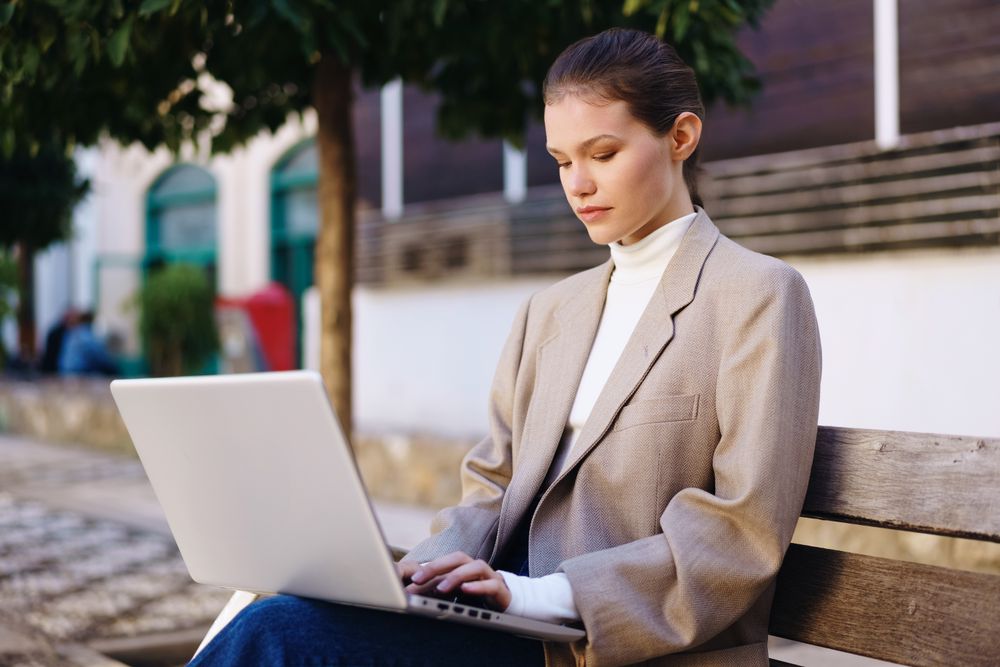A young professional is actively engaged in work on a laptop in an urban park setting