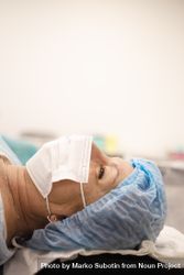 Woman in hair net and facemask lying down pre-surgery, vertical 5wea6b
