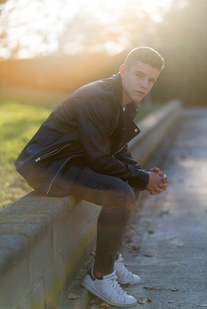 Teenage male wearing a leather jacket sitting on ledge outside