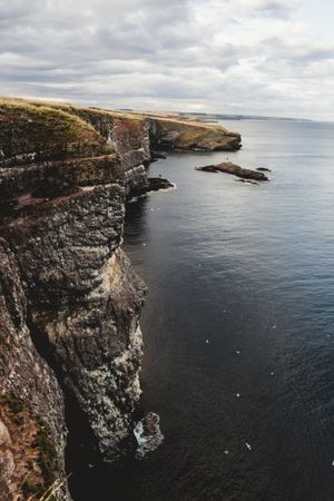 Rocky coast among tranquil ocean water in sunny day