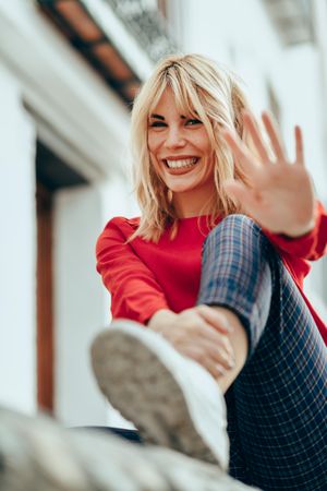 Happy blonde female with red shirt with palm out to camera, vertical