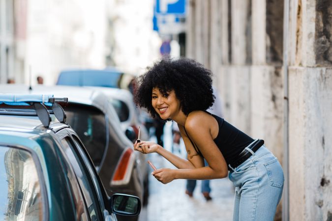 Black female applying lipstick outdoors
