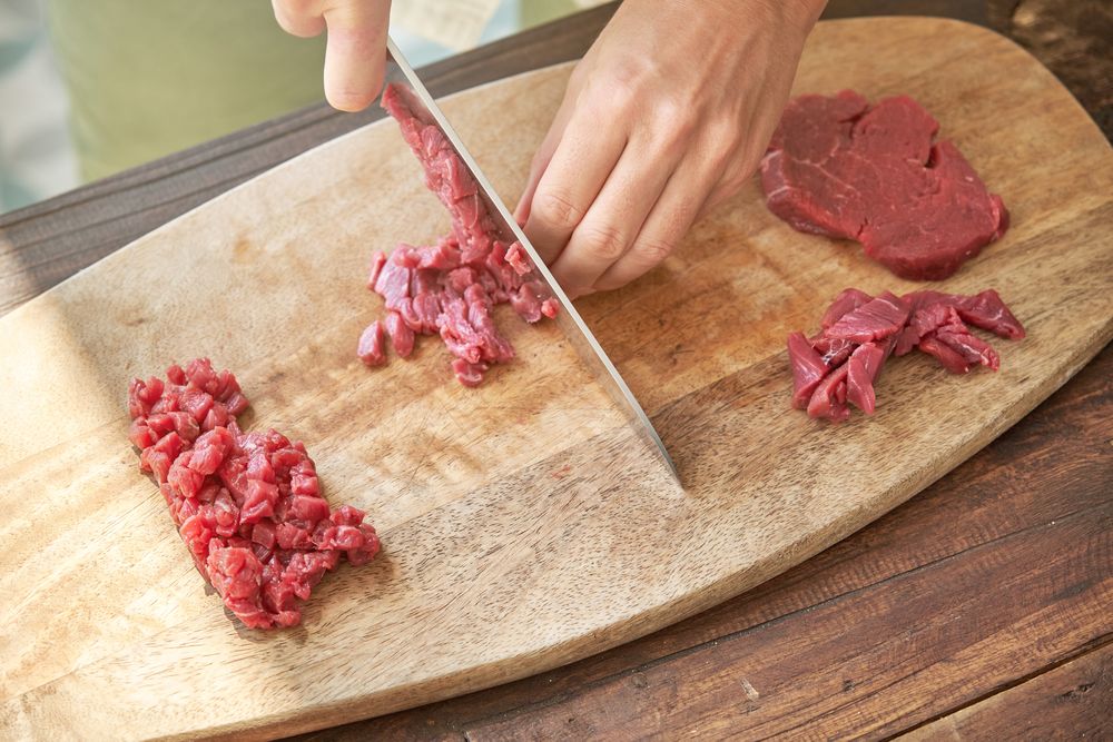 Crop cook chopping meat on wooden board