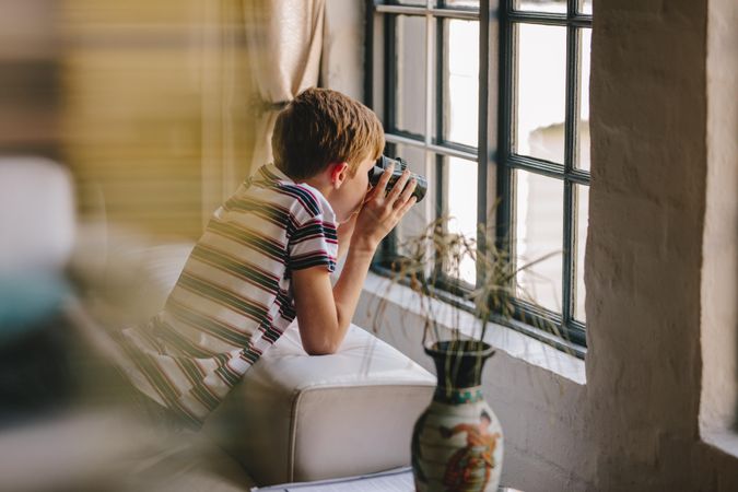 Boy on sofa looking outside window using binoculars