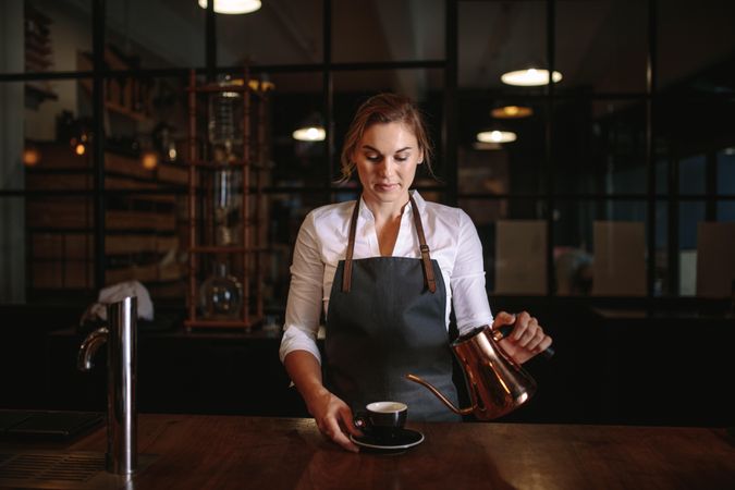 Woman coffee shop owner pouring coffee into a cup