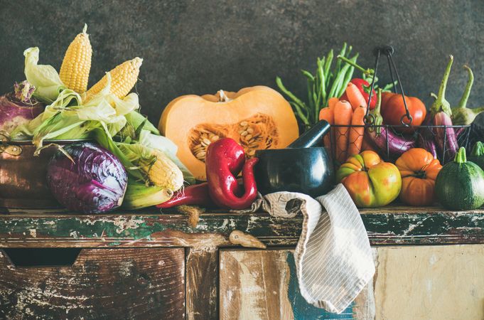 Fresh produce on wooden counter with dark background with central squash, corn, cabbage