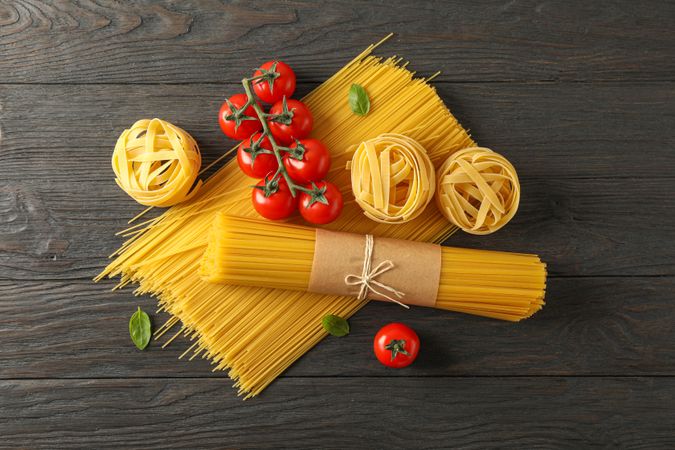 Composition with pasta, tomatoes and basil on wooden background, space for text and top view