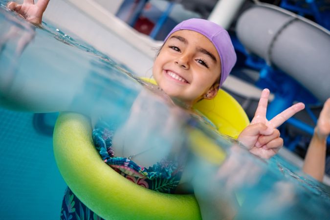 Happy girl gesturing V sign in swimming pool