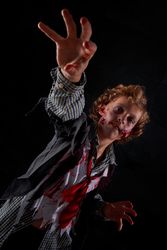Vertical photo of a boy disguised as a zombie with blood with his arms raised trying to catch something in front of him