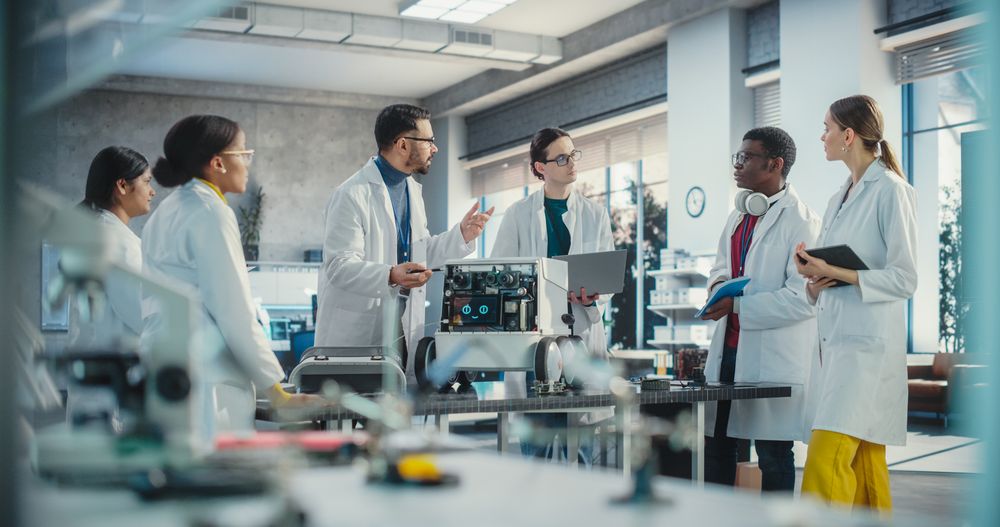 Diverse Team of Industrial Robotics Specialists Gathered Around a Table With a Mobile Robot.