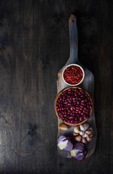 Wooden bread board with bowl of kidneys, red peppercorns, bulb of garlic and onion half