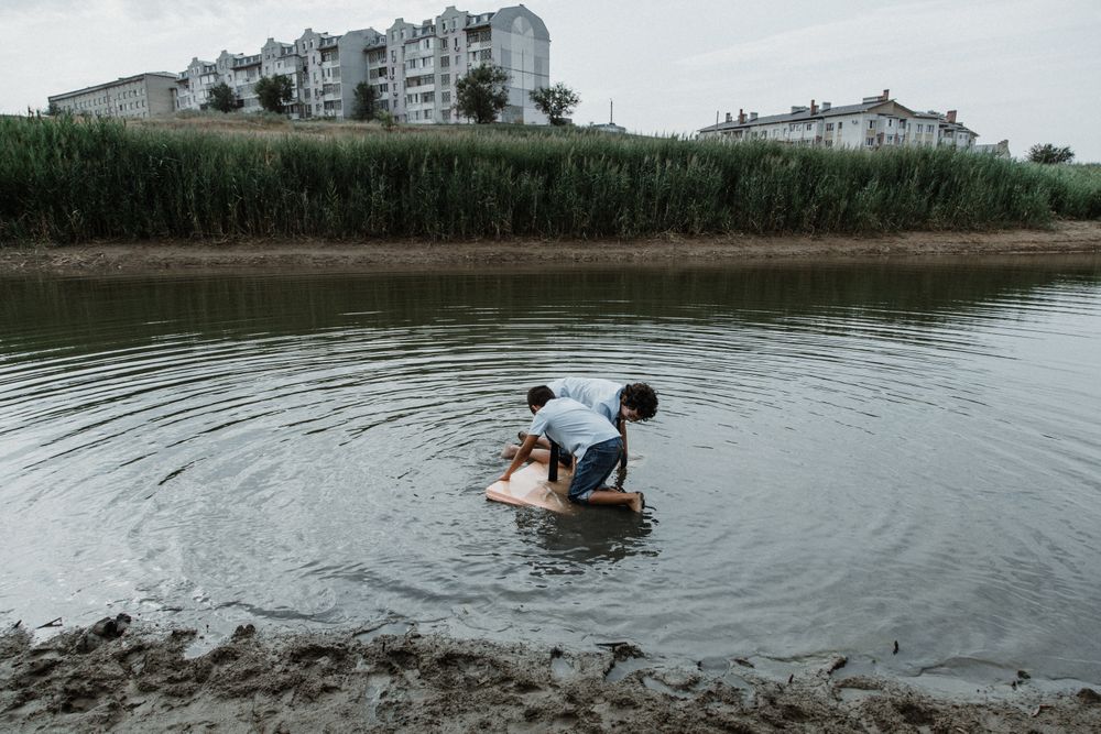 Kid brothers playing in dirty pond in daylight