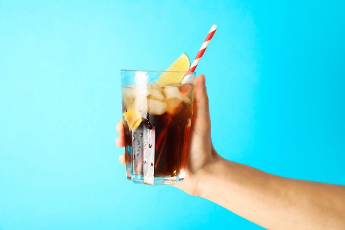 Female hand holding a glass with ice cola, tubule and lime slice