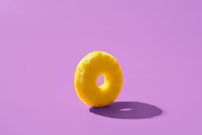 Pineapple ring balanced on purple background with shadow