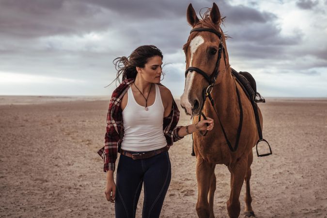 Portrait of woman leading her   horse on the beach with storm clouds