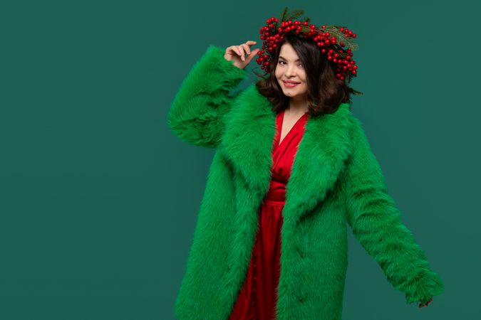 Woman in green coat and red berry wreath posing confidently.