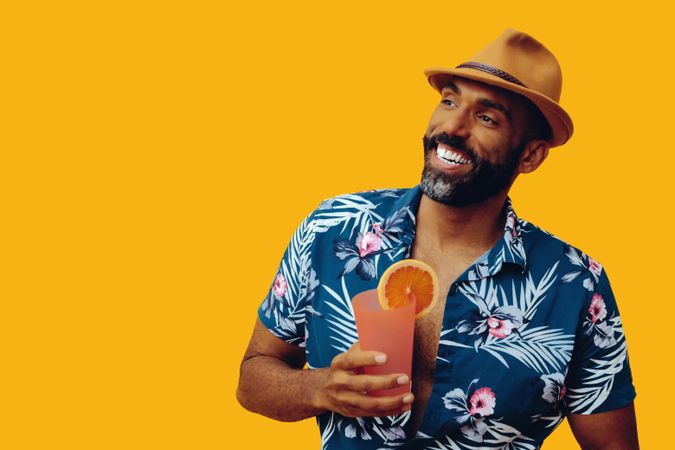 Happy male holding a cocktail while wearing colorful shirt with yellow background, copy space