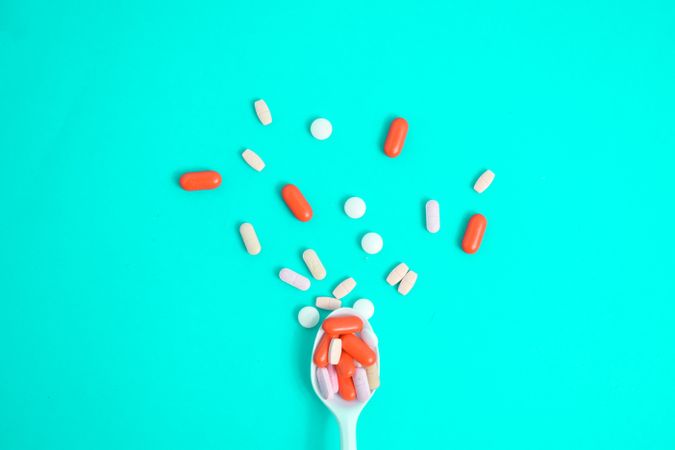 Spoon with scattered colorful tablets on green table