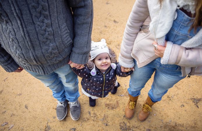 Happy girl looking up while holding her parents hand outside