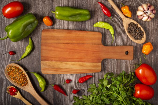 Empty cutting  board on the table with Ingredients for cooking. Tomatoes, various peppers, garlic and green peppers.