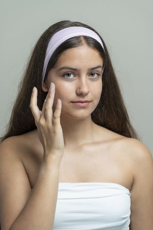 Beautiful young woman looking at camera while applying face cream or moisturizer