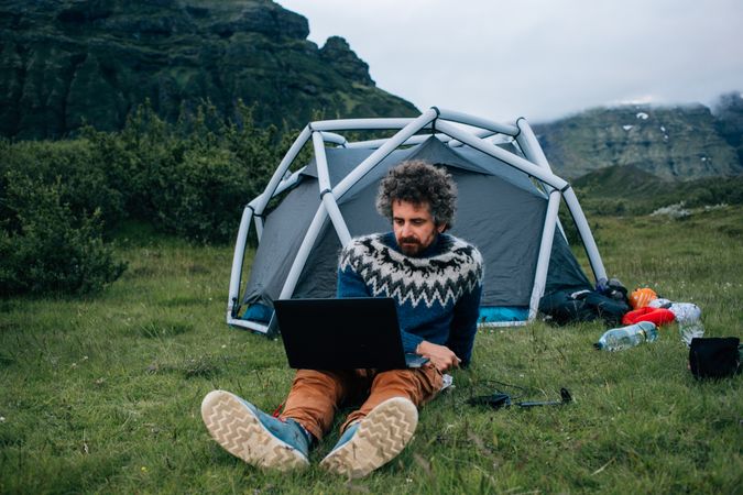 Man working on laptop in front of a campsite