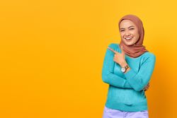 Muslim woman pointing to the side in yellow studio
