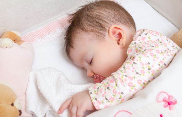 Baby sleeping soundly in a cot with pacifier and toy