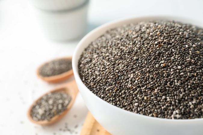Bowl and spoons with chia on plain background, close up