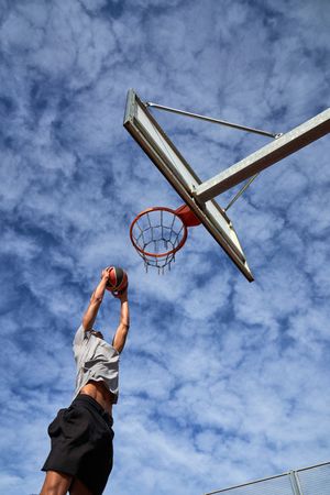 Man athlete jumping while dunking basketball against sky