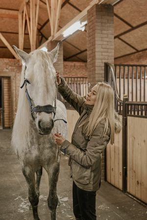 Woman hugging horse with long mane in face in stable