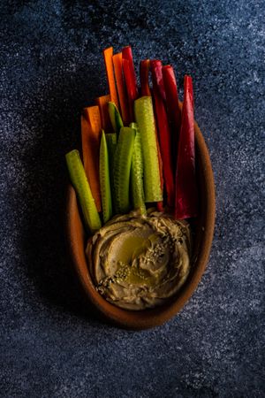 Top view of hummus dish served with chopped veggies on grey counter