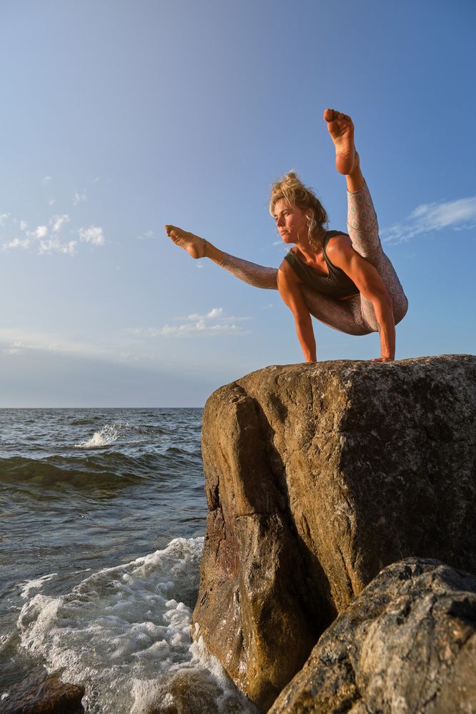 Woman balancing in Tittibhasana while practicing yoga on rock