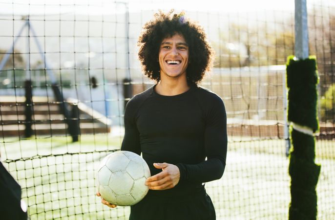 Athletic man holding soccer ball and smiling while at practice