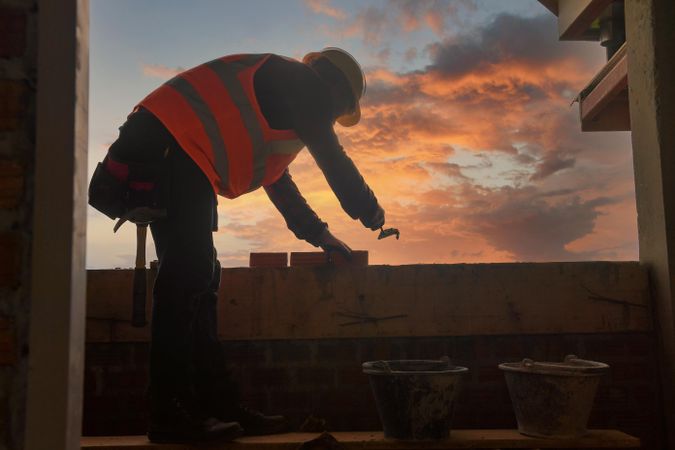 Man in orange vest building a wall at sunset
