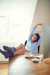 Woman at her office desk stretching her arms up with feet on desk, vertical