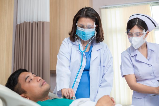 Female physician using stethoscope examine to sick man with nurse