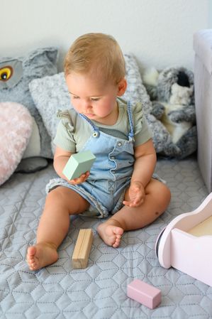 Baby playing with toy blocks on bed in daytime
