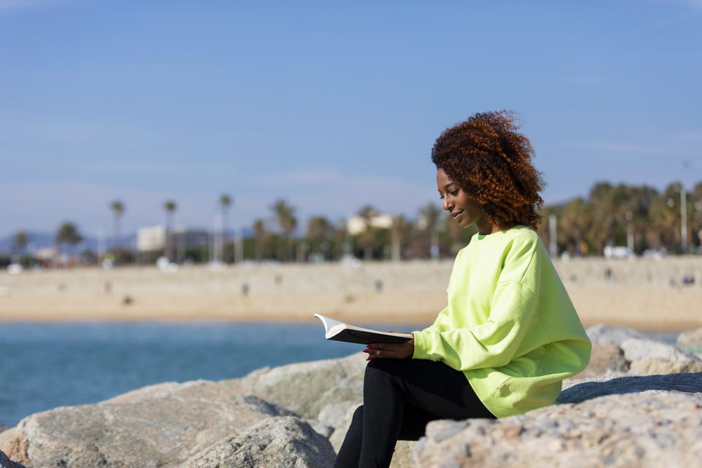 Female in bright green shirt sitting on the coast with a book