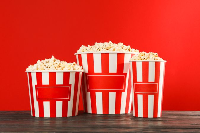Striped buckets with popcorn against red background, space for text