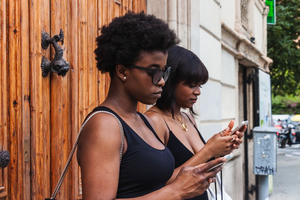 Black females using smartphones while standing on street