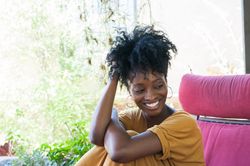 Woman with curly bun and bright smile sitting under covered patio area looking away