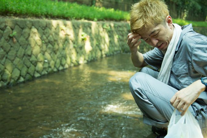 Side view of man in work suit crouching beside stream river