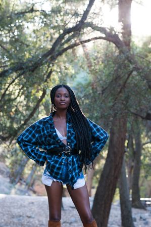 Fashion shot of woman standing in the woods with a flannel shirt smiling at camera