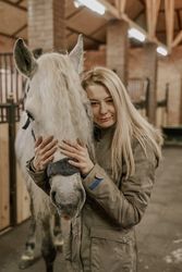 Woman hugging horse with long mane in face in stable
