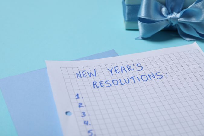 Gift box and paper with list on blue background, close up