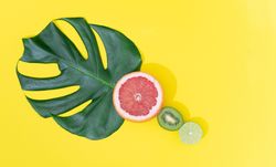 Monstera leaf with red grapefruit, lime and kiwi on bright yellow background