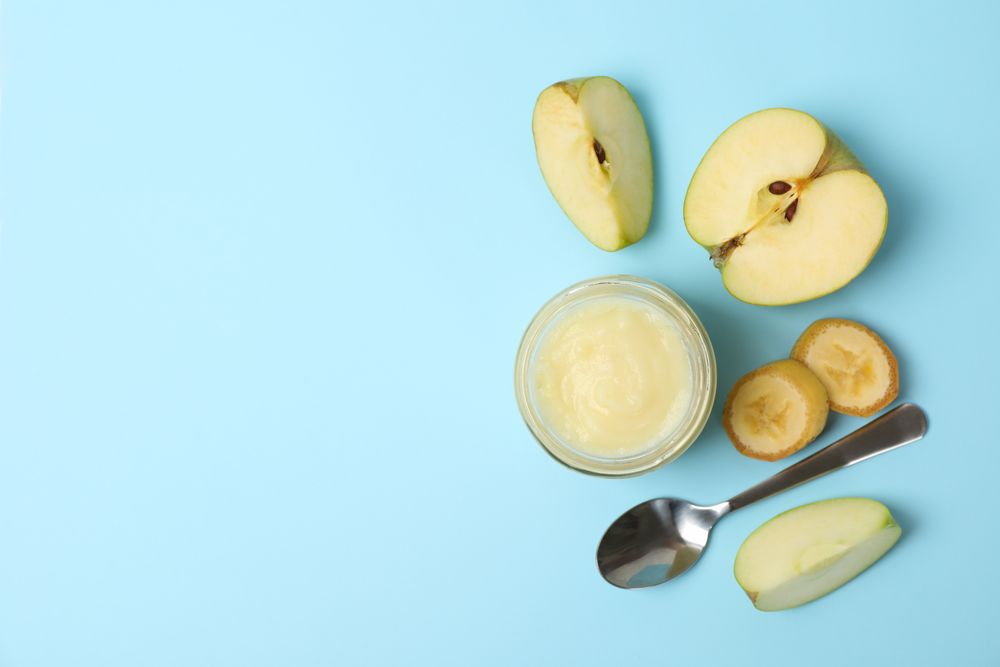 Glass jar with apple puree on blue background, top view