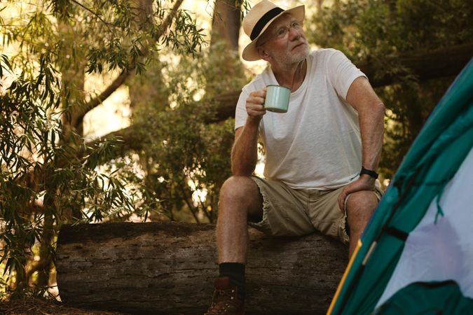 Older man sitting on a log with a cup of coffee