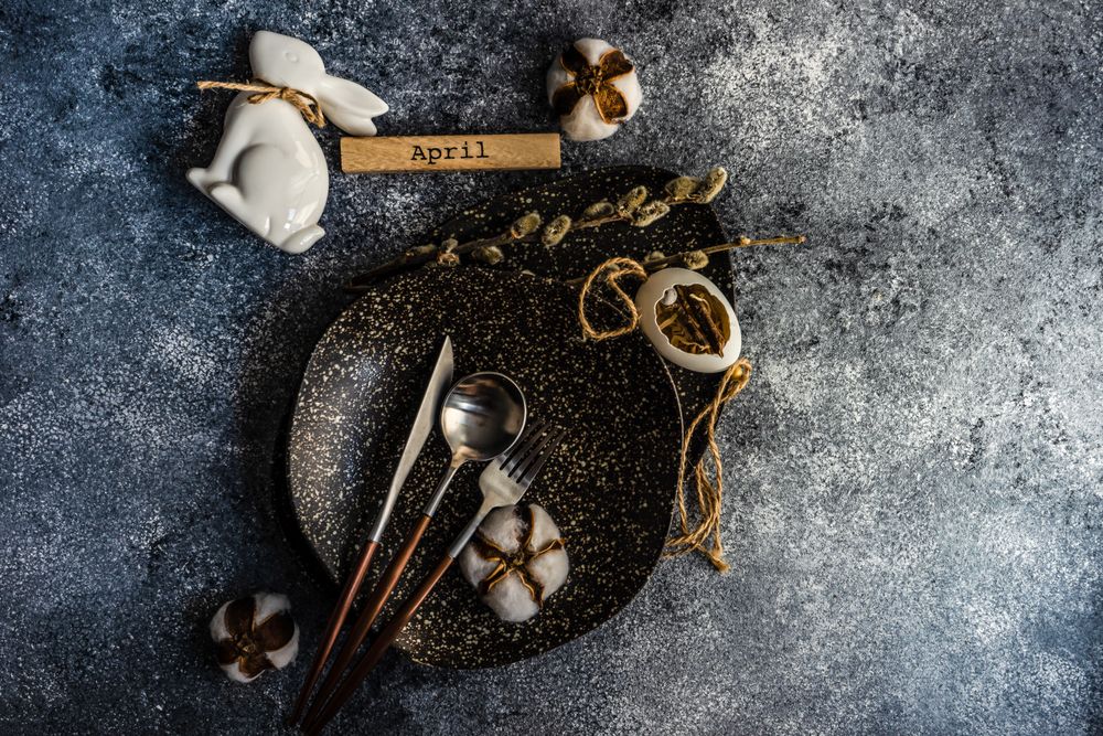 Top view of Easter table setting with cotton in dark bowl with rabbit & egg decor on grey counter